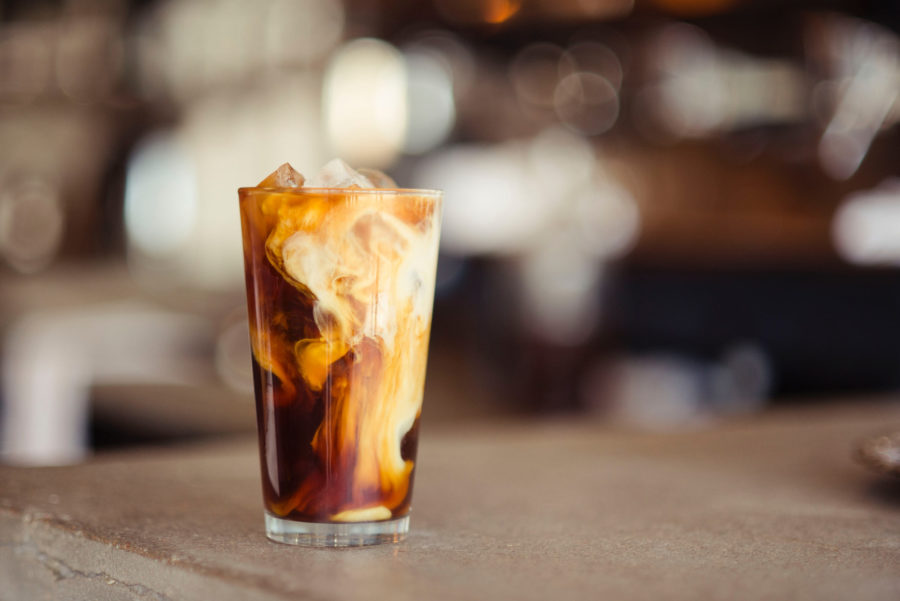 A glass of cold-brew coffee, served over ice, with a swirl of cream.