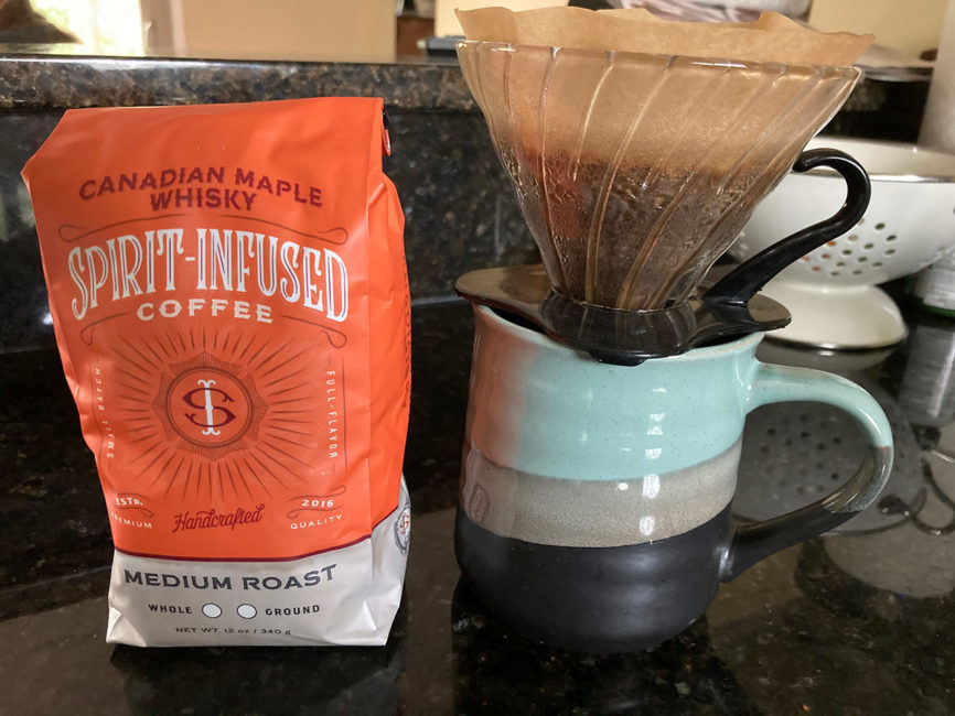 A bag of Fire Department Coffee's Maple Whiskey infused coffee next to a pour-over being made