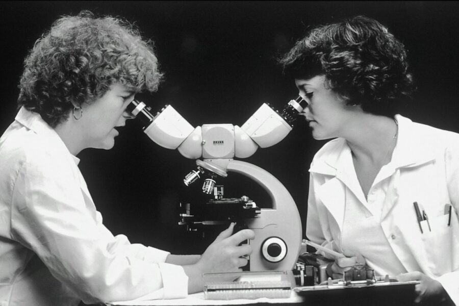 Black and white photo of two female-presenting scientists looking into adjoining microscopes